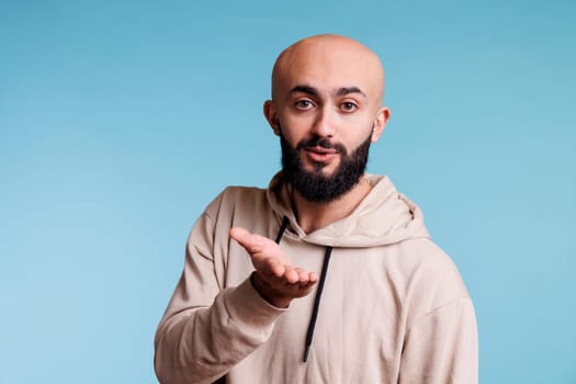 Arab man blowing air kiss with charming smile and looking at camera with flirty emotions. Romantic arabian bald bearded person expressing love and affection gesture studio portrait