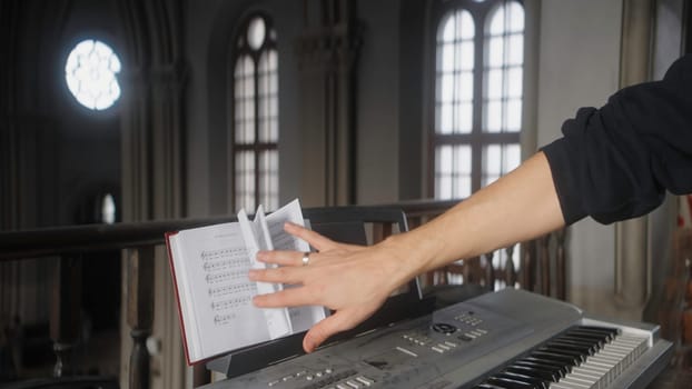 Man with sheet music and piano. Action. Man flips through music book on synthesizer. Close-up of musician on synthesizer in church.