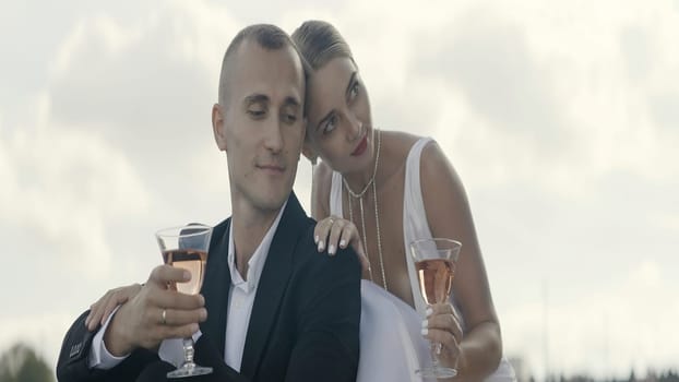 A dreaming couple. Action. A beautiful woman with her hair pulled back and a man who are hugging and drinking champagne from glasses. High quality 4k footage