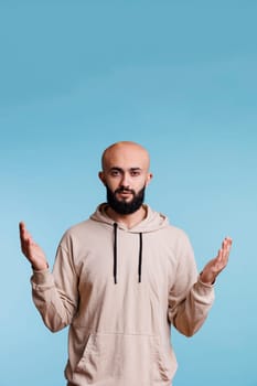 Arab man praying in spiritual gesture with raised hands while looking at camera with calm facial expression. Young person pleading and asking for blessing with open arms studio portrait