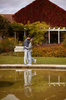 A couple in love hugs on the shore of a city pond in the European town. love story against the backdrop of autumn nature. romantic ambiance, couple goals, outdoor romance, seasonal charm, love in the city, autumnal vibes, European town, city pond, affectionate bonding, love story