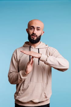 Young arab man taking break while showing time out gesture portrait. Person in casual hoodie clothes stopping communication with interruption signal and looking at camera