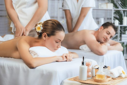 Caucasian couple customer enjoying relaxing anti-stress spa massage and pampering with beauty skin recreation leisure in day light ambient salon spa at luxury resort or hotel. Quiescent