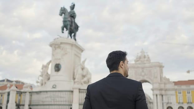 Rear view of joyful middle aged businessman in suit walking outdoors in city square. Action. People and urban background concept