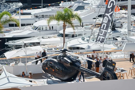 Monaco, Monte Carlo, 27 September 2022 - Rich clients visitors examine a helicopter standing on the deck of a yacht club, the largest fair yacht show, port Hercules, yacht brokers, sunny weather. High quality photo