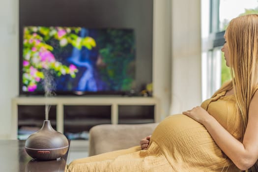 A blissful pregnant woman immerses in relaxation, savoring the soothing aroma from a diffuser while indulging in a calming TV video, embracing tranquility during her pregnant journey.