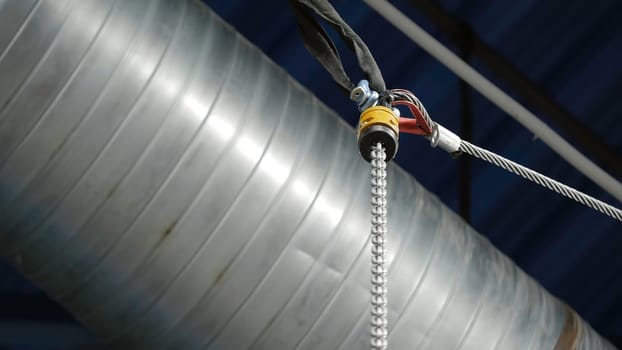 Bottom view of the suspension metal cable on th background of the ceiling and ventilation pipe. Technological details of the industrial room.