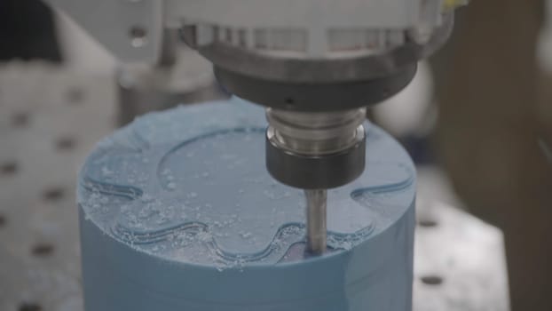 Industrial milling machine at work with blue wax candle blank. Close up of milling machine making beautiful ornament on wax figure or candle.