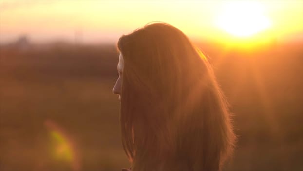 Woman enjoys warm summer sunset. Beautiful woman on background of sunset rays of sun.