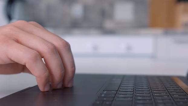 Side view of hand using touch pad of black laptop keypad. Close up of a keayboard and man hands working on modern computer on blurred background.