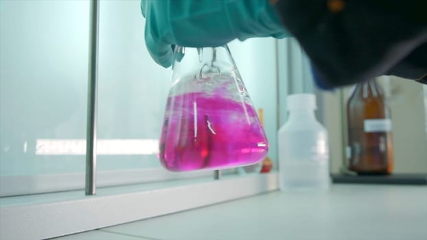 Close-up of flask with chemical liquid. Clip. Laboratory assistant conducts experiments with chemical liquid that changes colors. Chemical process in transparent flask in laboratory.