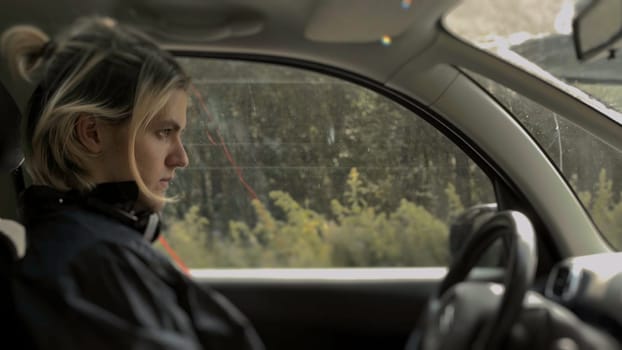 Guy is sitting behind wheel of car. Stock. Modern sad guy is sitting in car and waiting. Teenager is sitting at wheel by road and waiting.