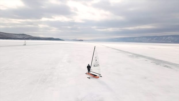 Aerial view of a man standing near the iceboat on the frozen Baikal lake. Flying over the icy water surface with ice yachts, winter sport and active lifestyle concept.