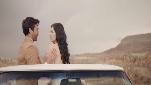 Side view of caring and loving couple standing on the mountain top near the car. Action. Man and woman enjoying stone valley, man embracing his lady