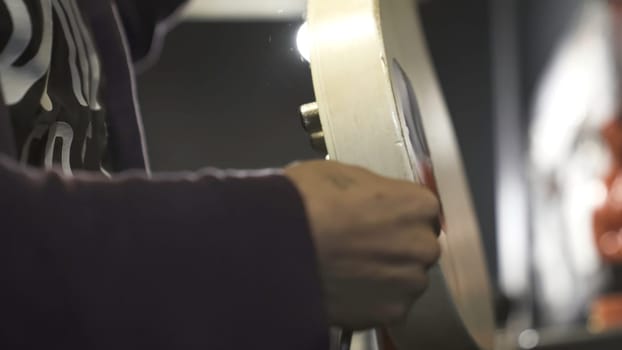 Close up of a man putting jack cable into electric guitar. Male musician holding white electric guitar and audio jack cable on blurred background, music concept.