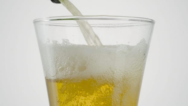 Close-up of beer being poured into clear glass. Action. Beer is poured into transparent glass on white isolated background. Beer is poured into glass.