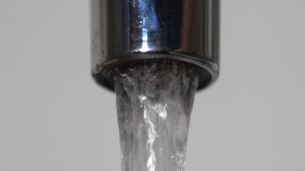 Extreme close up of the water flowing from the faucet. Chrome water tap spout with flowing fresh water.