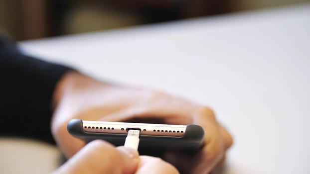 Close up of hand inserting a USB cable charger into a mobile phone. Close up mans hand inserting a charger into a smart phone through a lightning cable.