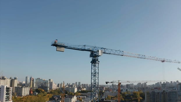 Top view of construction crane on background of city on sunny day. Stock footage. Construction cranes at height with view of city to horizon. Construction crane on background of modern city on sunny summer day.