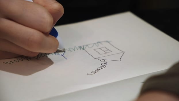 Child drawing a picture of his family and a gouse in notebook, close up. Small kid using a pen to draw a sketch of his mom and dad near the house.