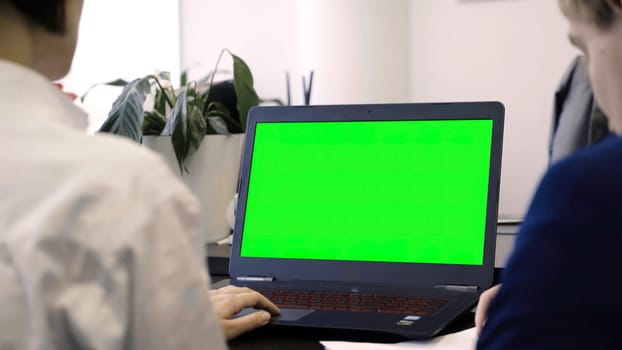 View of employees and green laptop screen. View from back of office workers on laptop with green screen. Concept of office work.