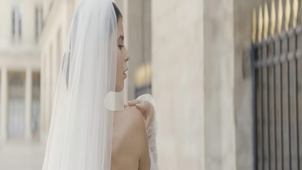 Beautiful female model in a transparent veil. Action. A young woman with bare shoulders and a veil made of mesh posing in the fresh air. High quality 4k footage