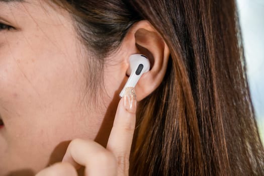 Close up of Happy female touching earbuds to control next listen song on mobile phone in living room at home, Lifestyle woman wearing wireless earphones listening to favorite song on her smartphone