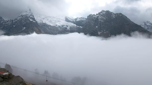 Timelapse of moving clouds in mountains with snow. Creative. Covering clouds in snowy rocky mountains. Cumulus clouds below snowy peaks of rocky Mountains in cloudy weather.