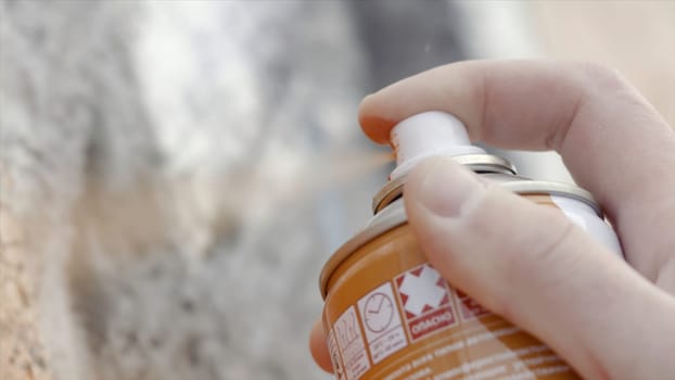 Close-up of artist draws street art spraying spray paint. Action. Stained fingers of artist hold spray can with colored paint on concrete wall. Street artist in process of creating graffiti.