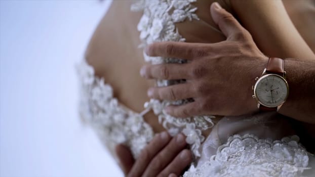 Close-up of husband's hands hugging wife. Action. Husband gently touches his wife's waist in white wedding dress. Concept of wedding.