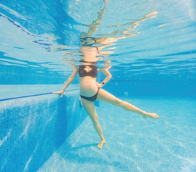 Embracing aquatic fitness, a pregnant woman demonstrates strength and serenity in underwater aerobics, creating a serene and empowering image in the pool.