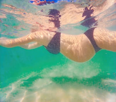 In an ethereal underwater scene, a pregnant woman gracefully floats, embodying the beauty of maternity beneath the tranquil surface of the sea.