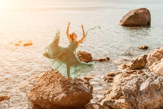 Woman green dress sea. Woman in a long mint dress posing on a beach with rocks on sunny day. Girl on the nature on blue sky background