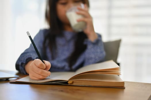 Select focus on hands of Asian school girl doing homework at dining table