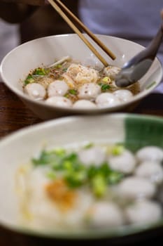 Close up of White rice noodle, clear soup, Meat Balls  with ingredients in white bowl.