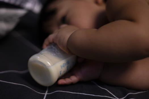 Baby with bottle lying in comfortable bed. Baby Drinks Milk From Bottle.