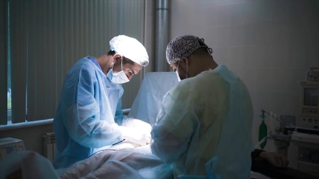 Close-up of professional surgeons performing surgery on person. Action. Two specialized surgeons carefully perform operation under anesthesia.