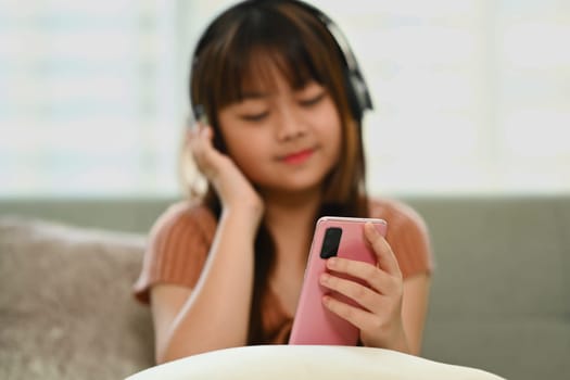 Cute Asian girl wearing headphone watching video on mobile phone.