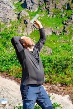 In the midst of mountainous terrain, a tourist enjoys a soothing moment by pouring cold water to cool down on a hot sunny day. The refreshing scene captures the essence of nature's tranquility.