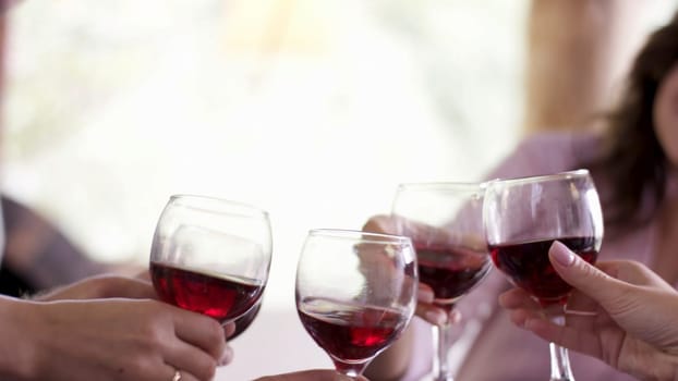 People hands clinking glasses of red wine, close up. Group of fiends drink red wine from transparent glasses and cheering, the concept of party and celebration.