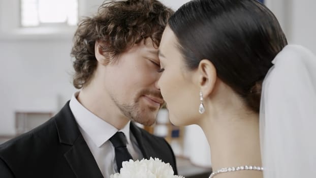 Side view of a loving couple kissing each other during marriage process in a church. Action. Groom and bride first kiss