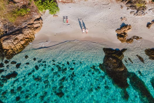 Koh Samet Island Thailand, aerial drone view at a couple of men and woman on the beach of Samed Island in Thailand with a turqouse colored ocean and a white tropical beach in the morning sun