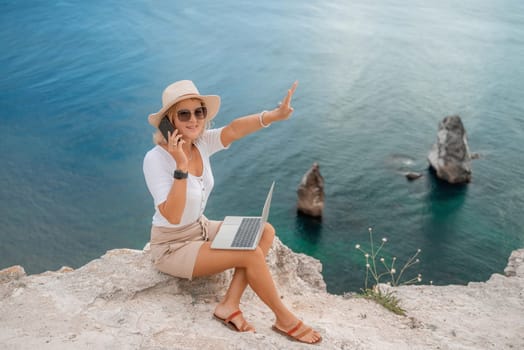 Freelance women sea working on the computer. Good looking middle aged woman typing on a laptop keyboard outdoors with a beautiful sea view. The concept of remote work