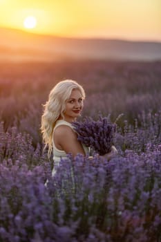 Blonde woman poses in lavender field at sunset. Happy woman in white dress holds lavender bouquet. Aromatherapy concept, lavender oil, photo session in lavender.