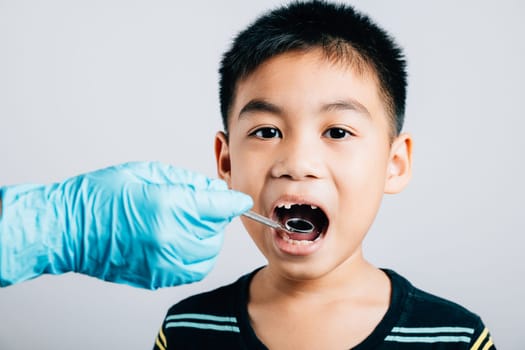 Pediatric dentist examines a child's mouth after removal of a loose milk tooth. Dental assistant assists in examination with dental instruments. Doctor uses mouth mirror to checking teeth cavity