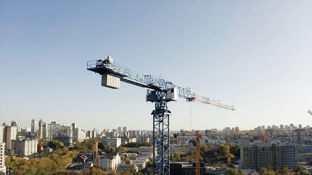 Construction site on the city background. Stock footage. Aerial view of a crane and the city buildings with green trees