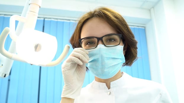 Patient point of view of a dentist examining patient mouth, modern dentistry concept. Young female dentist looking at the patient and turning the lamp.