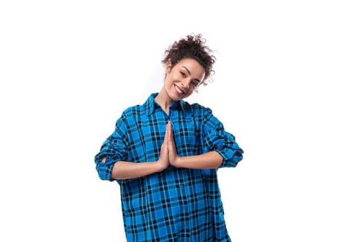 european young lady with curly ponytail hairstyle dressed in a blue shirt put her hands together.