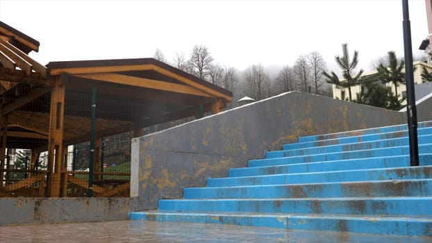 Wooden pavilion in raining season located near concrete stairs on grey heavy sky background. Covered gazebo under the rain in late autumn.