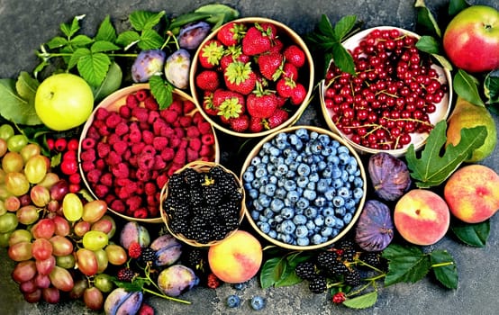 A variety of summer berries - raspberries, strawberries, blueberries, cherries, currants, plums - in cups on a wooden table